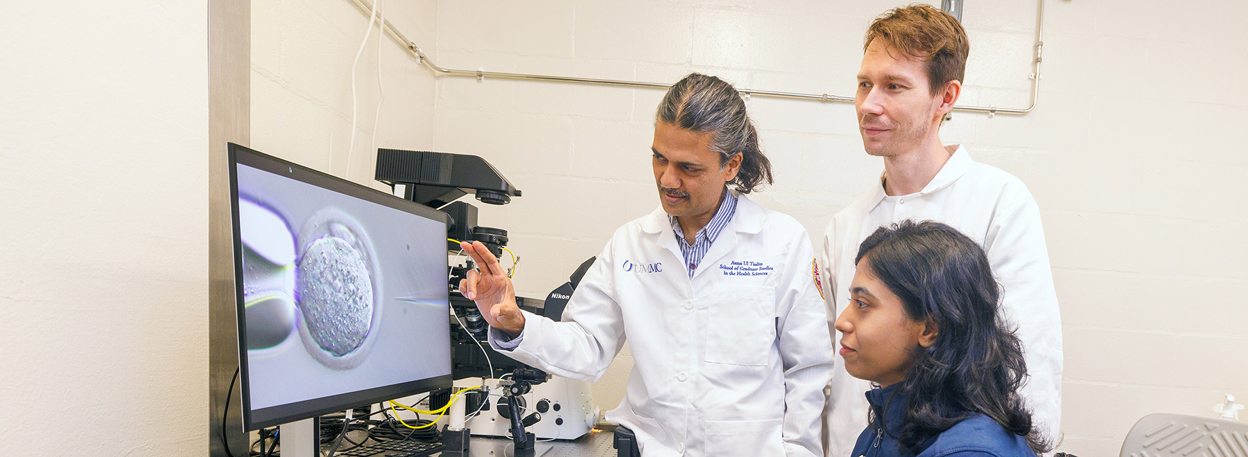 three researchers looking at an image of a cell on a monitor